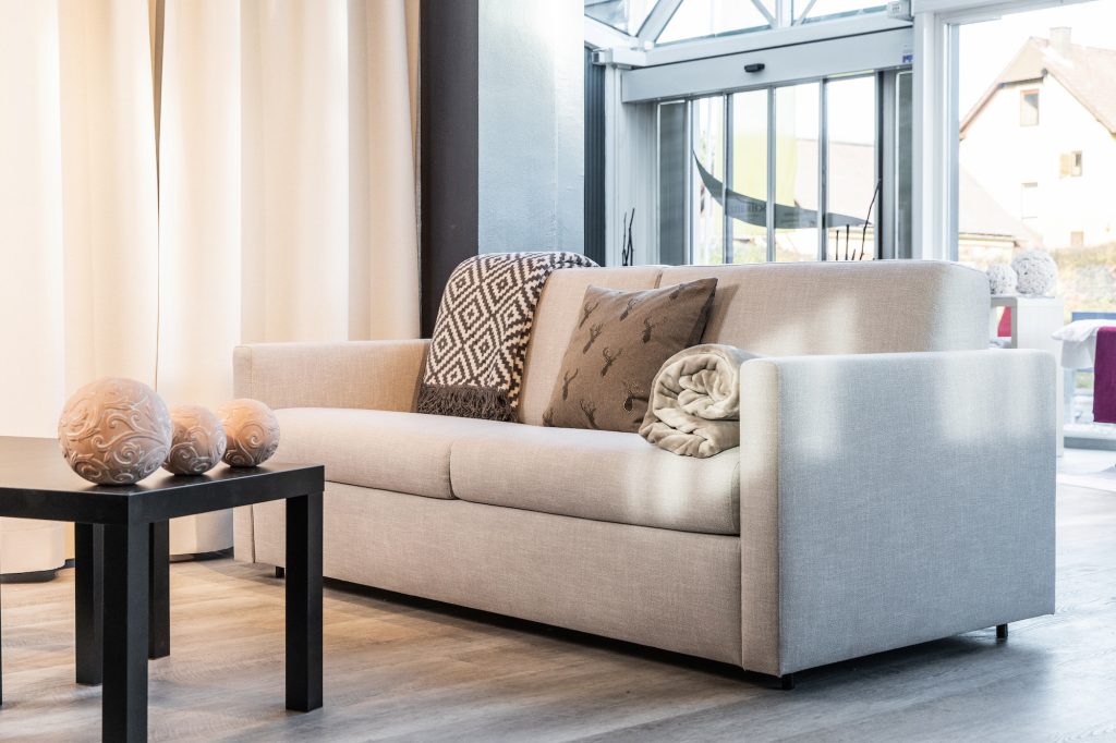 Helle Ausziehcouch mit Dekokissen und Plaid in modernem Wohnraum