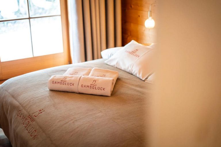 Hotelbett mit hochwertiger Bettwäsche und personalisierten Handtüchern „Chalet Gamsglück“