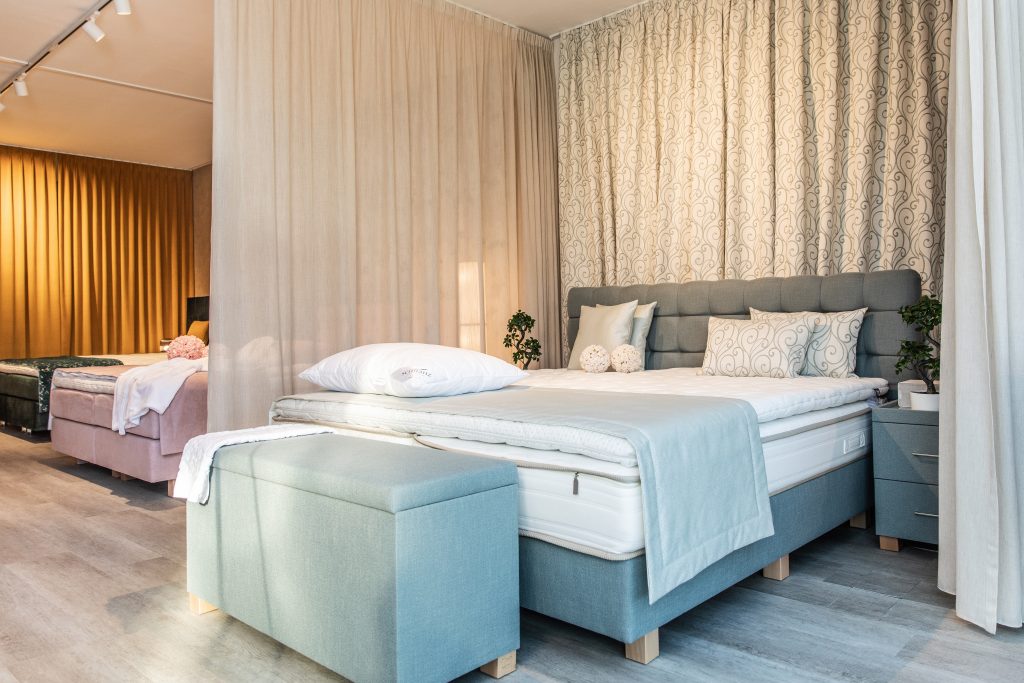 Modern eingerichtetes Schlafzimmer mit Boxspringbett, hellen Textilien und dekorativen Vorhängen